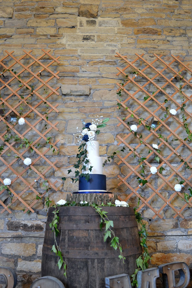 navy white wedding cake with rambling foliage displayed on log slice and beer barrel