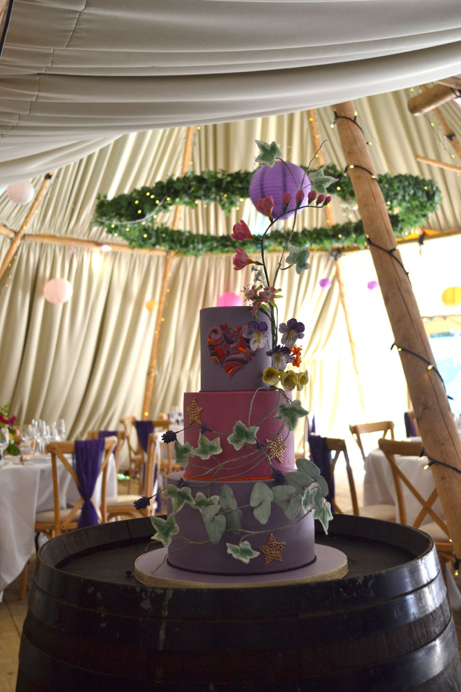 vibrant purple pink wedding cake with rambling stems and woodland flowers displayed on beer barrel stand